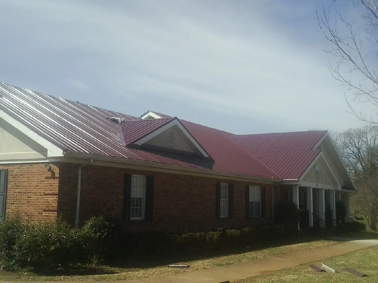 Red metal roof with gabled entries on a long brick building, from a Hail Damage Roof Repair job in Clara City