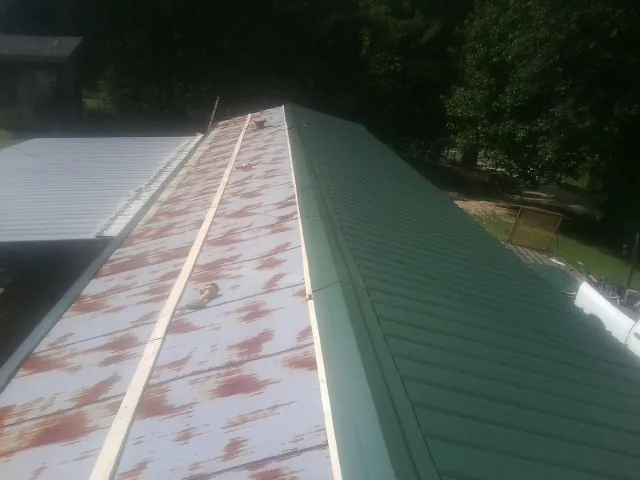 Old rusted panels beside newly installed green metal roofing — Wind Damage Roof Repair by Roofing Brothers in Clara City