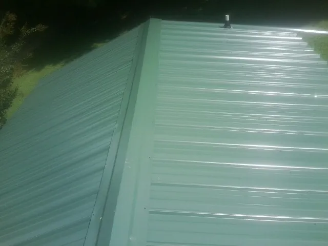 New green metal panels meeting at the ridge of a roof — Flat Roof Repair work by our crew in Clara City