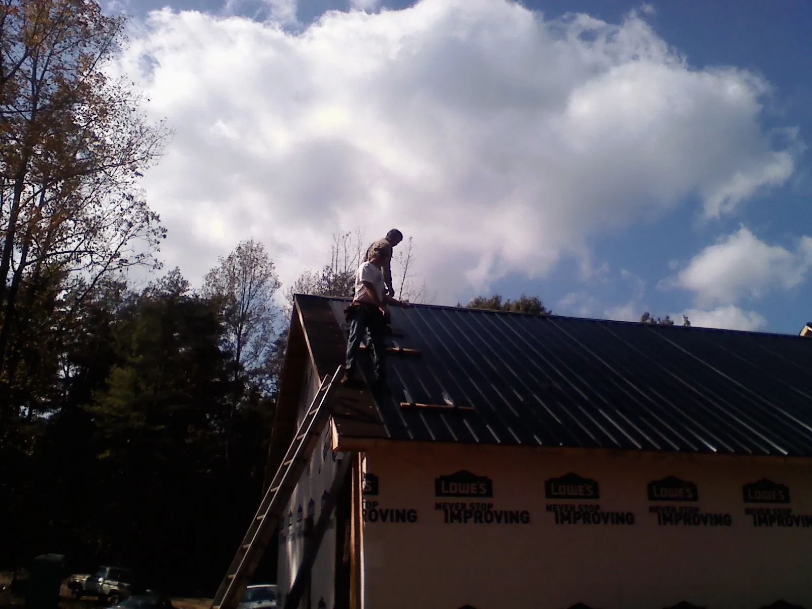Roofer fastening dark metal panels high against a cloudy sky, from a Roof Inspection job in Clara City