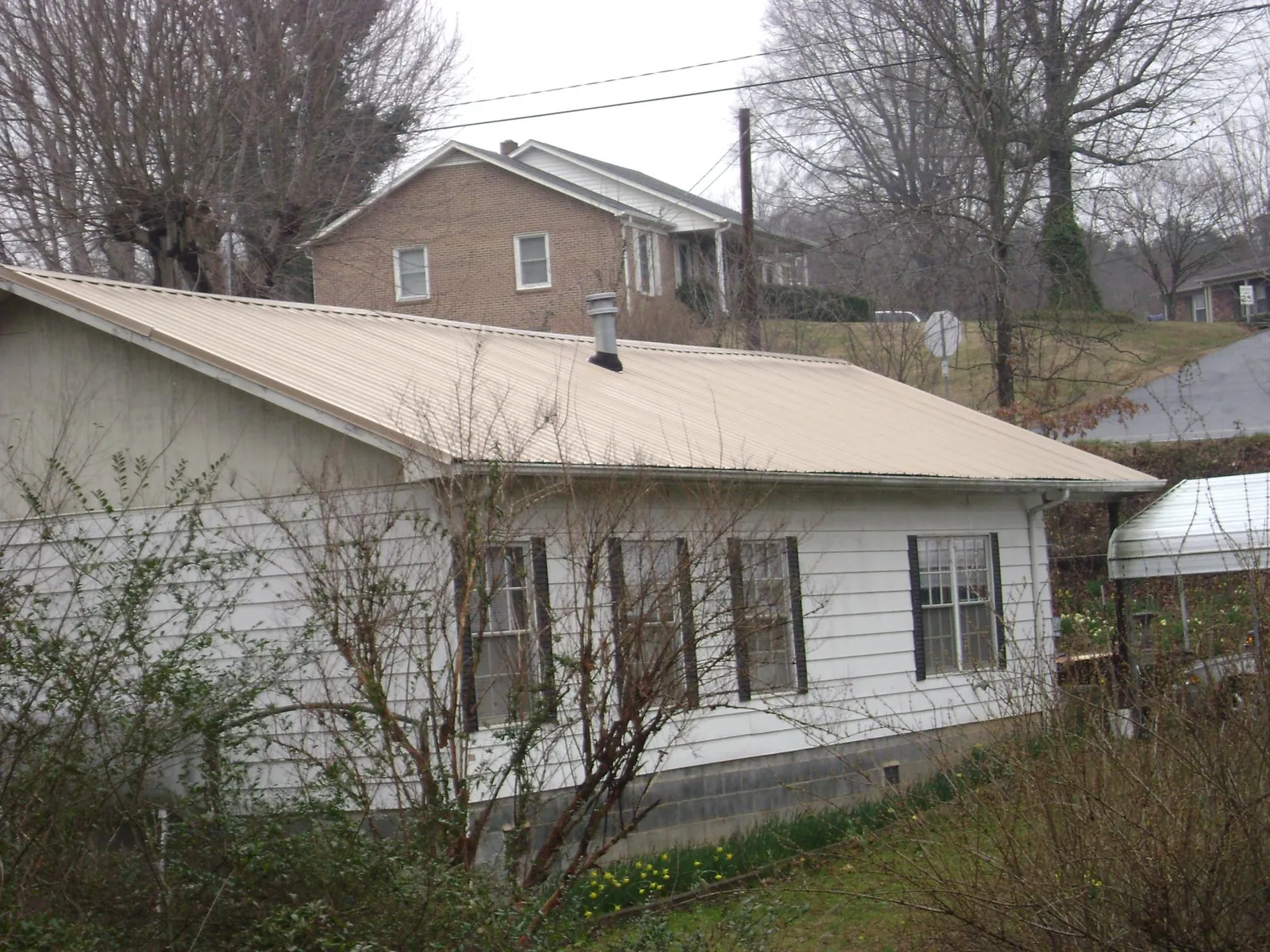 Tan metal roof on a white sided house set into a hillside — Commercial Roofing by Roofing Brothers in Clara City
