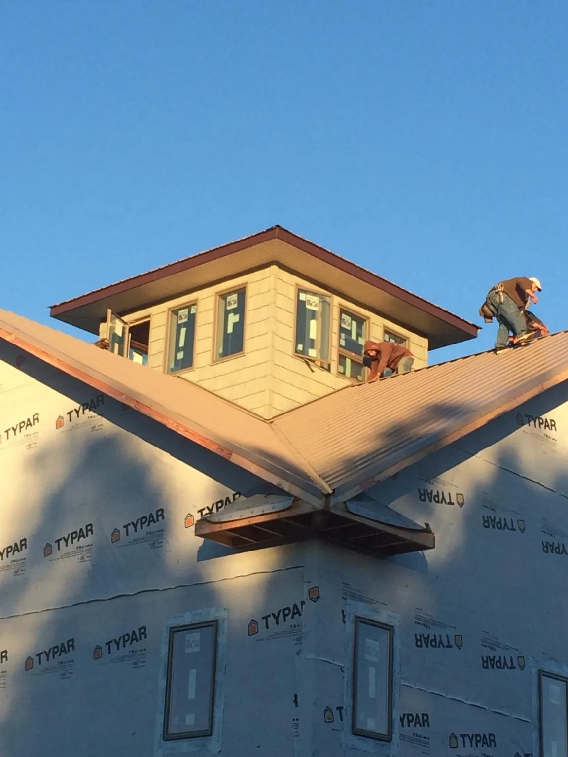 Roofers working around a rooftop cupola on a new metal roof at sunset — Roof Waterproofing in Clara City by Roofing Brothers